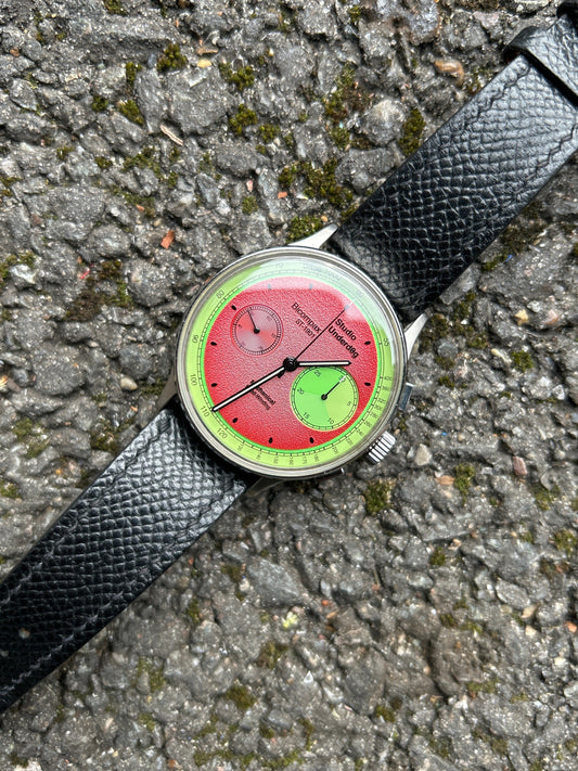 Wristwatch with a unique red and green face on a textured surface